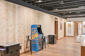 Una stanza con pareti rivestite in legno, un tavolo da ping pong, una macchina arcade blu e un piccolo angolo bar.