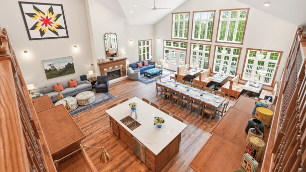 A spacious living area with a large dining table, a kitchen island, and a view of the outdoors through large windows.