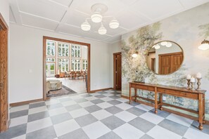 A checkered floor, a wooden console table with a mirror, and a door leading to a dining area.