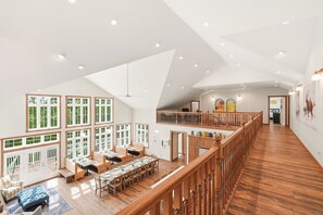 A spacious interior with a high ceiling, wooden flooring, a dining area, and a staircase leading to an upper level.