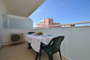 Ein Balkon mit Tisch für zwei Personen, einem Stuhl und Blick auf ein Hotel im Hintergrund.