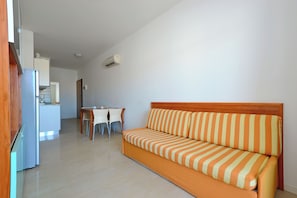 A modern living room with a sofa, a dining table with chairs, and a kitchen area in the background. - Holiday Home Just 50m From the Beach (Lignano Sabbiadoro)