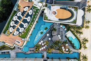 Vista aérea de um resort com várias piscinas, quadra de tênis e um anfiteatro circular.