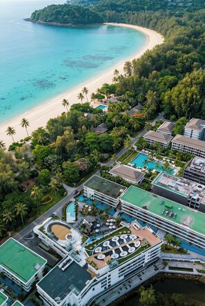 Luchtbeeld van een resort met een strand, zwembad en weelderige begroeiing.