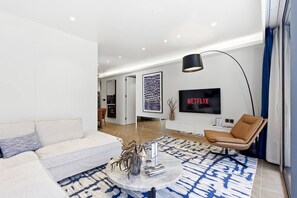 A modern living room with a white sofa, a coffee table, a leather armchair, a patterned rug, and a flat-screen TV mounted on the wall. - Private Pool/ 200 m to the Beach Design Apartment (Choeng Thale)