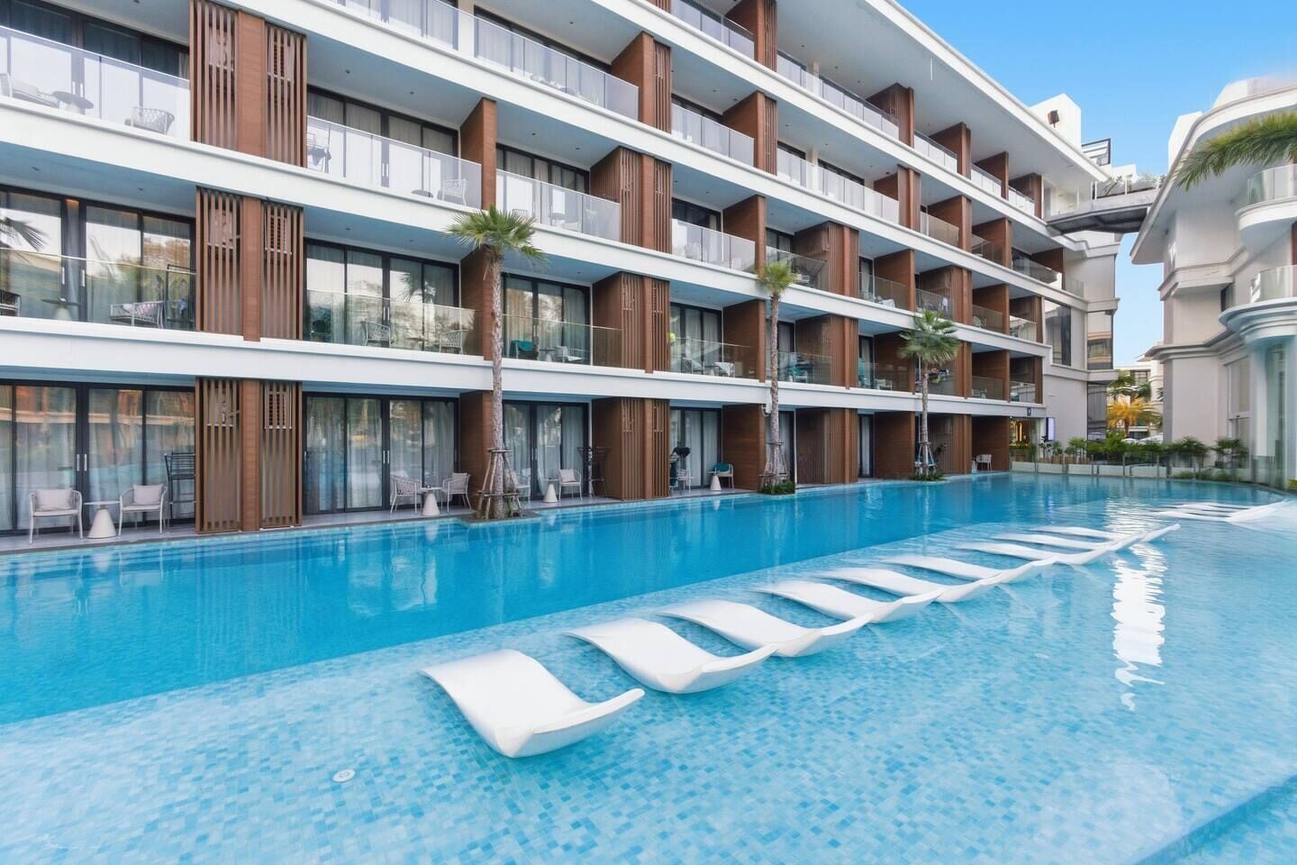 A multi-story hotel with a swimming pool, outdoor seating, and palm trees.