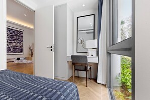 Ein Hotelzimmer mit einem Bett, einem Schreibtisch mit Stuhl, einem Spiegel und einem Fenster mit Blick auf Grünflächen.