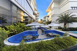 En uteplats med blå sittmöbler, parasoller och en pool.