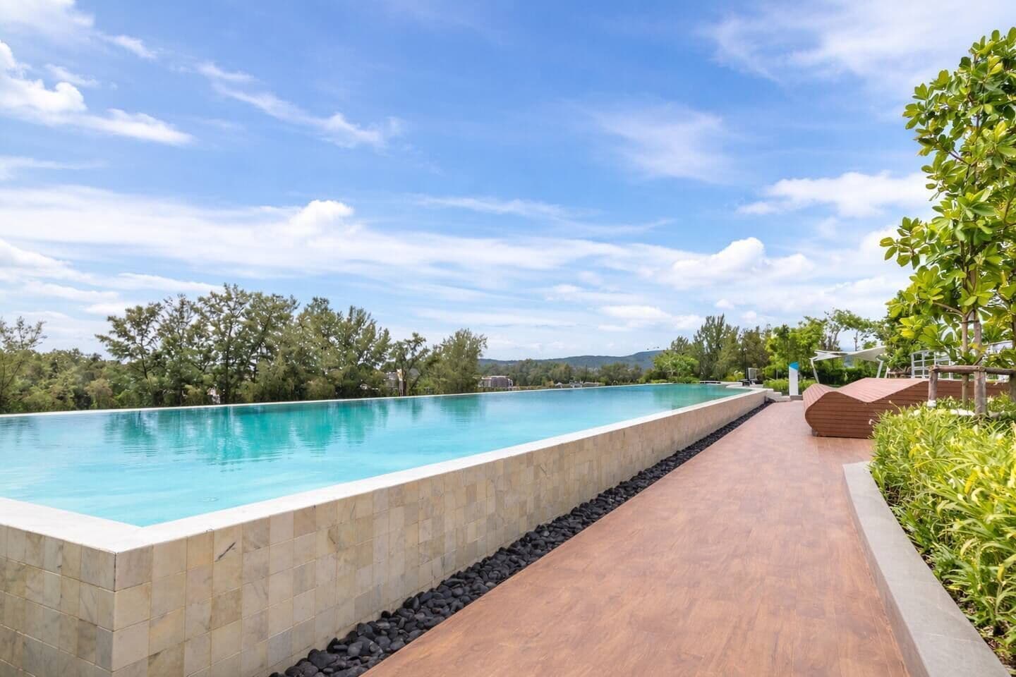 Una piscina rettangolare con bordo in pietra, circondata da un solarium in legno e un vialetto con ciottoli.