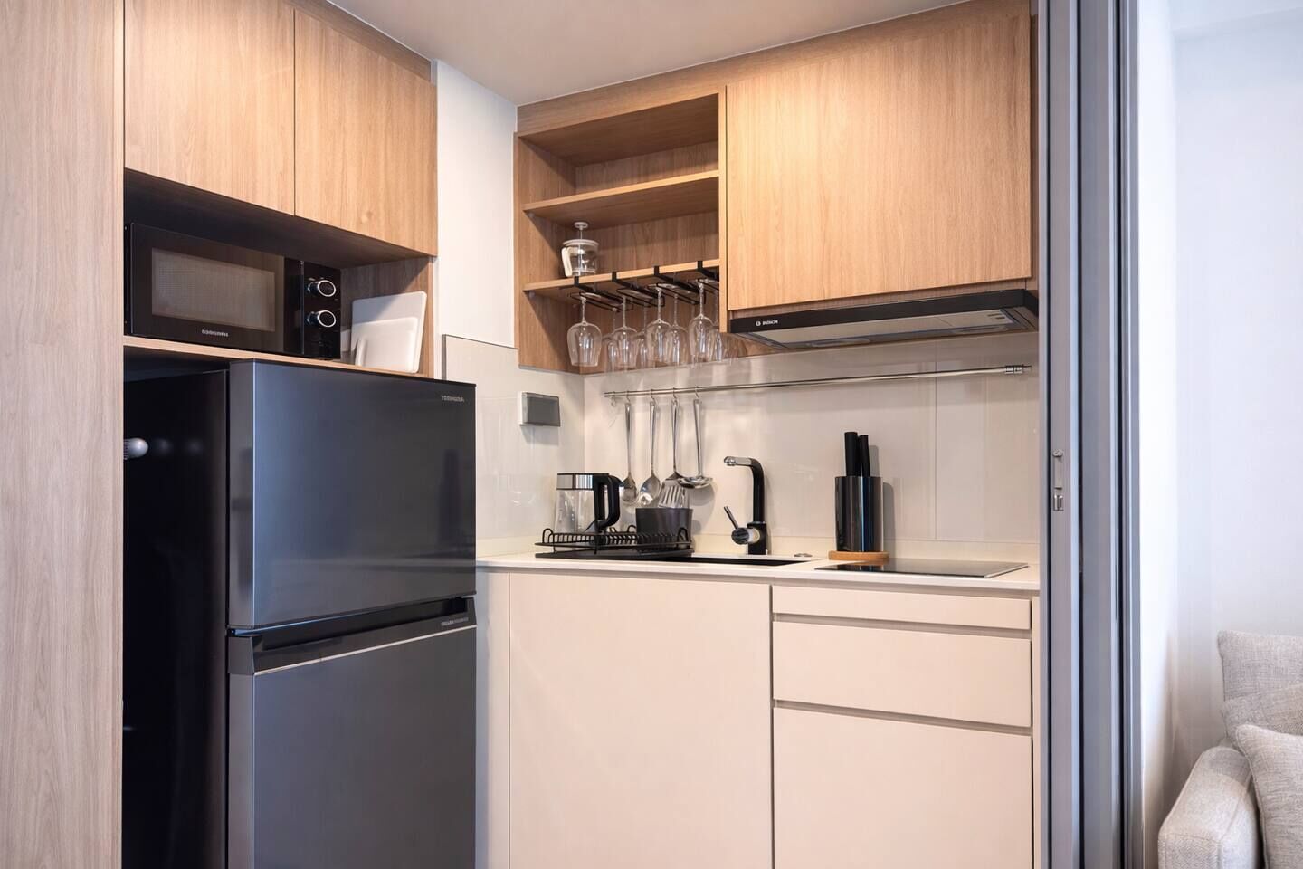 Une cuisine compacte équipée d’un réfrigérateur intégré, d’une machine à café et d’un porte-verres à vin.