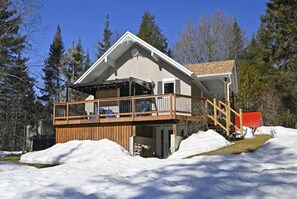 A cabin with a wooden deck, a covered porch, and a snow-covered landscape.