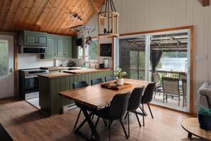 A modern kitchen with a wooden ceiling, green cabinets, and a dining area with a wooden table and chairs.