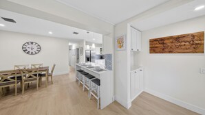 Una cucina moderna con mobili bianchi, un tavolo da pranzo in legno con sedie, un angolo bar con sgabelli e una sveglia a parete.