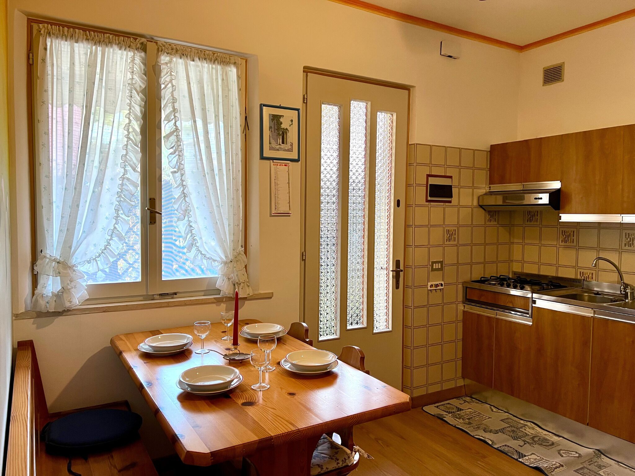 Un coin repas avec une table en bois dressée pour quatre personnes, une cuisine avec des placards en bois et une porte ornée de panneaux de verre décoratifs.