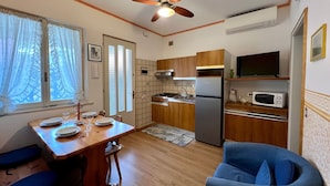 Une cuisine compacte avec des meubles en bois, un four à micro-ondes encastré, un réfrigérateur et un ventilateur de plafond.