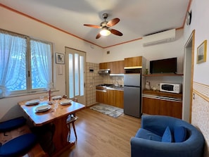 A compact kitchen with wooden cabinets, a built-in microwave, a refrigerator, and a ceiling fan. - Relax in our Charming Patio in Lignano (Lignano Sabbiadoro)