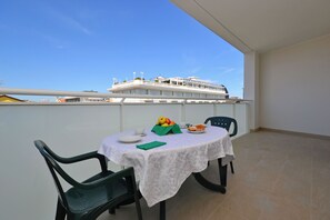 Ein Balkon mit Tisch für zwei Personen, Stühlen, einer Tischdecke und Blick auf ein Kreuzfahrtschiff.