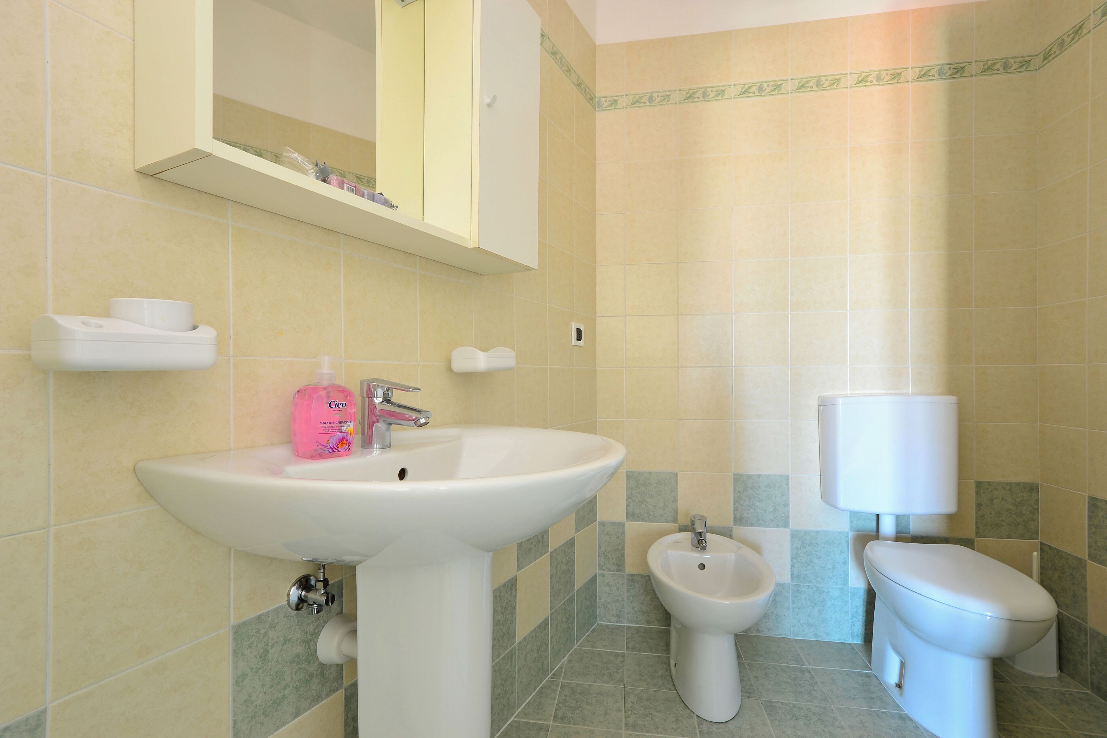 Et badeværelse med vask, bidet, toilet og et spejl over vasken.