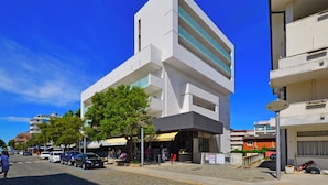 A modern building with a flat facade, large windows, and a tree in front. - Sweet Holiday Home Just 50mt From the Beach (Lignano Sabbiadoro)