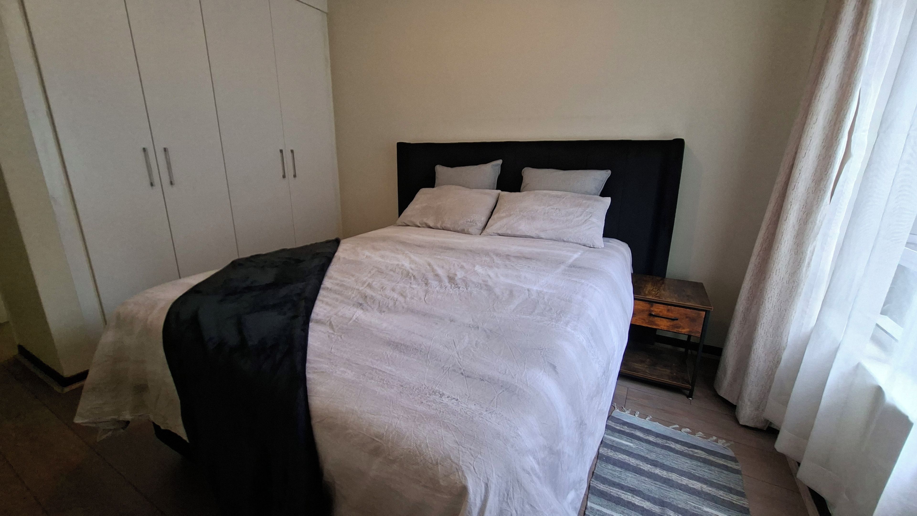 Ein Hotelzimmer mit Bett, Schrank, Nachttisch und einem Fenster mit Vorhängen.