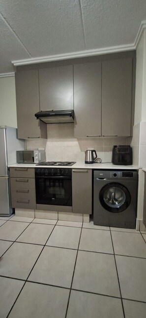A kitchen with a stove, microwave, oven, washing machine, and cabinets. - Serene Haven - Peaceful, Secure & Conviniently located apartment (Sandton)