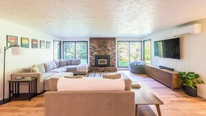 A living room with a sectional sofa, a fireplace, a TV, and large windows.