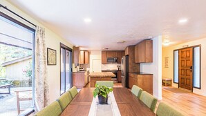 A spacious dining area with a long wooden table, green cushioned chairs, and a central potted plant.