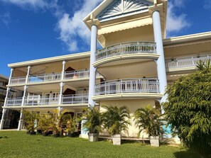 Ein mehrstöckiges Hotel mit Balkonen, einem gepflegten Rasen und tropischen Pflanzen.