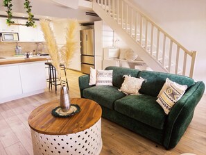 Ein modernes Wohnzimmer mit einem grünen Sofa, einem runden Holztisch und einem weißen Beistelltisch.
