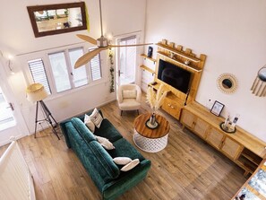 Ein Wohnzimmer mit einem grünen Sofa, einem runden Couchtisch, einem Fernseher auf einem Holzgestell und einem Deckenventilator.