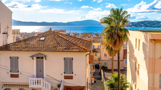 A coastal town with terracotta-tiled buildings, a palm tree, and a view of the sea. - Contemporary apartment with sea view - Private parking & Private boat (Sainte-Maxime)