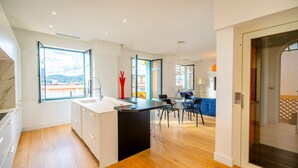 A modern kitchen with a large window, a dining area with a blue sofa, and a view of the cityscape. - Contemporary apartment with sea view - Private parking & Private boat (Sainte-Maxime)