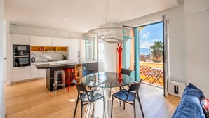 A modern kitchen with a dining area, large windows, and a view of a beach. - Contemporary apartment with sea view - Private parking & Private boat (Sainte-Maxime)