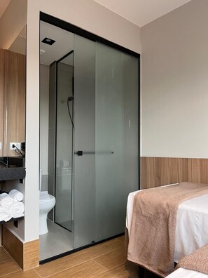 Un baño moderno con cabina de ducha de vidrio, inodoro y cama con toalla.