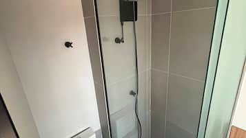 Casa de banho moderna com chuveiro de vidro, sanita e candeeiro no teto.