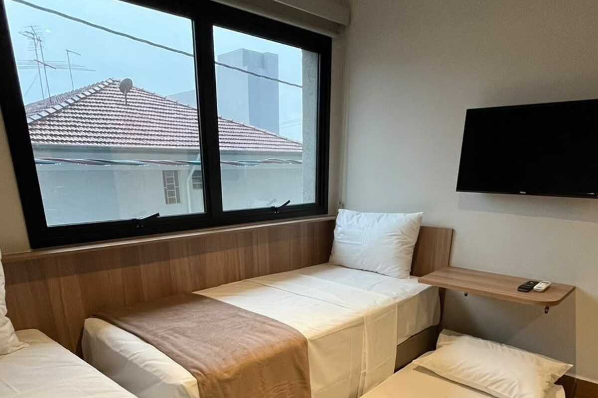 A hotel room with two beds, a TV mounted on the wall, and a window with a view of buildings.