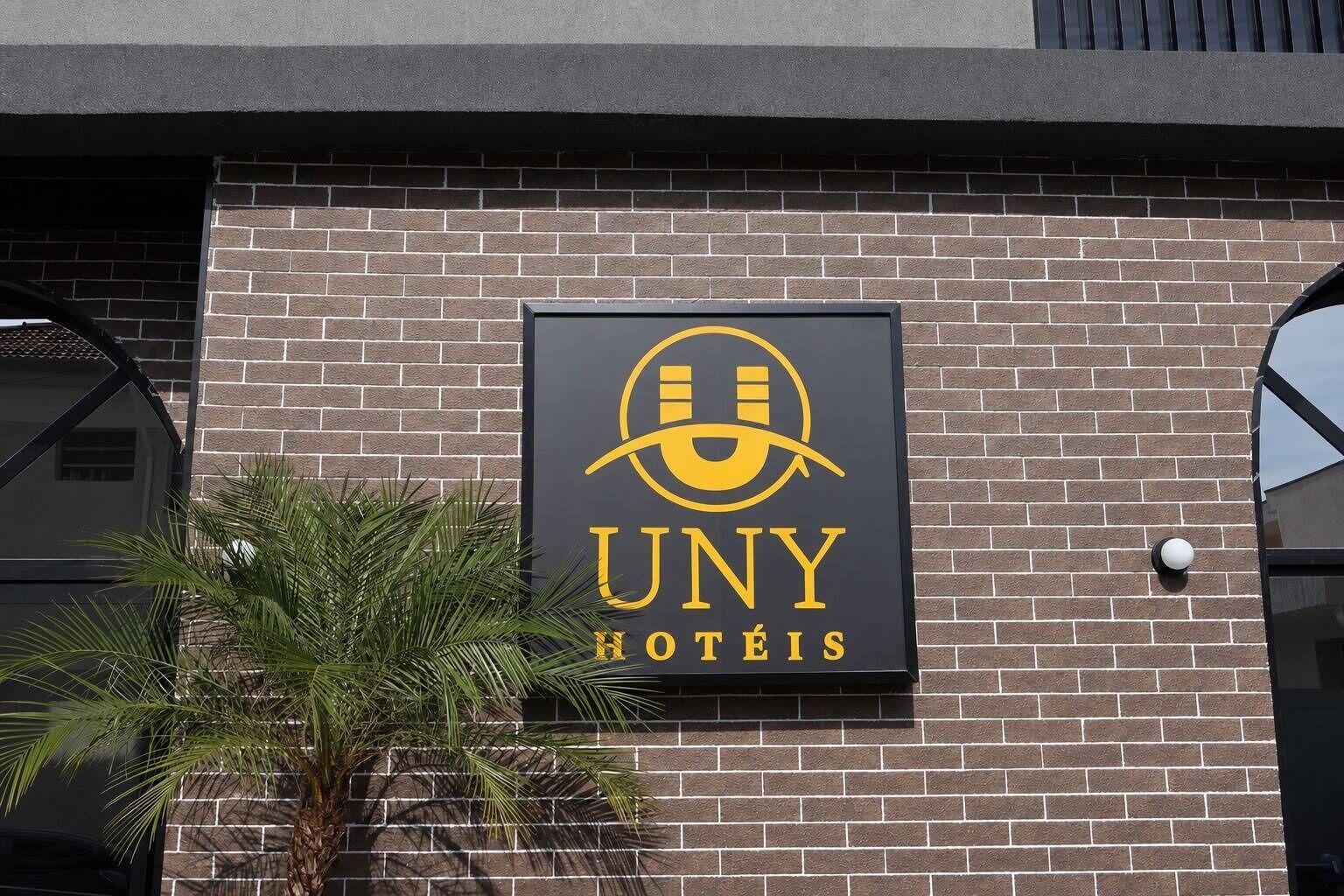 A hotel sign with the name 'UNY HOTÉIS' on a brick wall.
