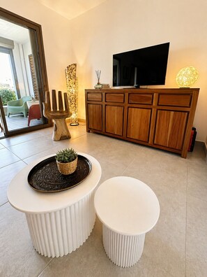 Ein modernes Wohnzimmer mit einem Holzkabinett, einem Flachbildfernseher, einer dekorativen Stehlampe und zwei weißen Poufs.