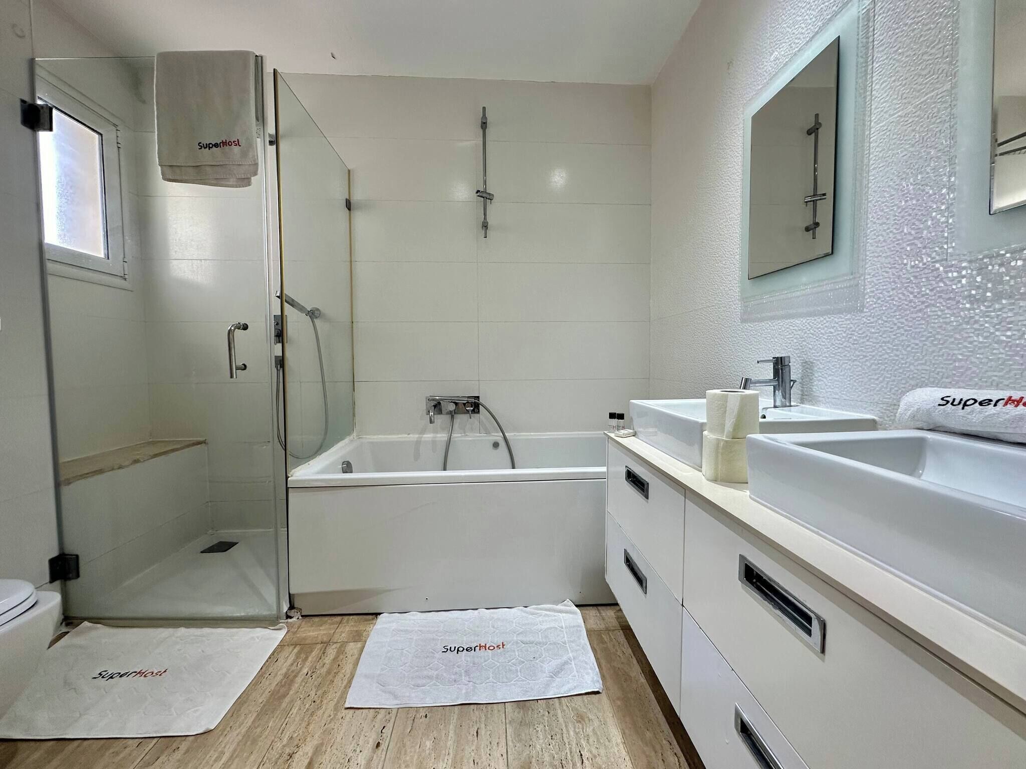 A modern bathroom with a glass shower enclosure, a bathtub, and a vanity with a mirror.