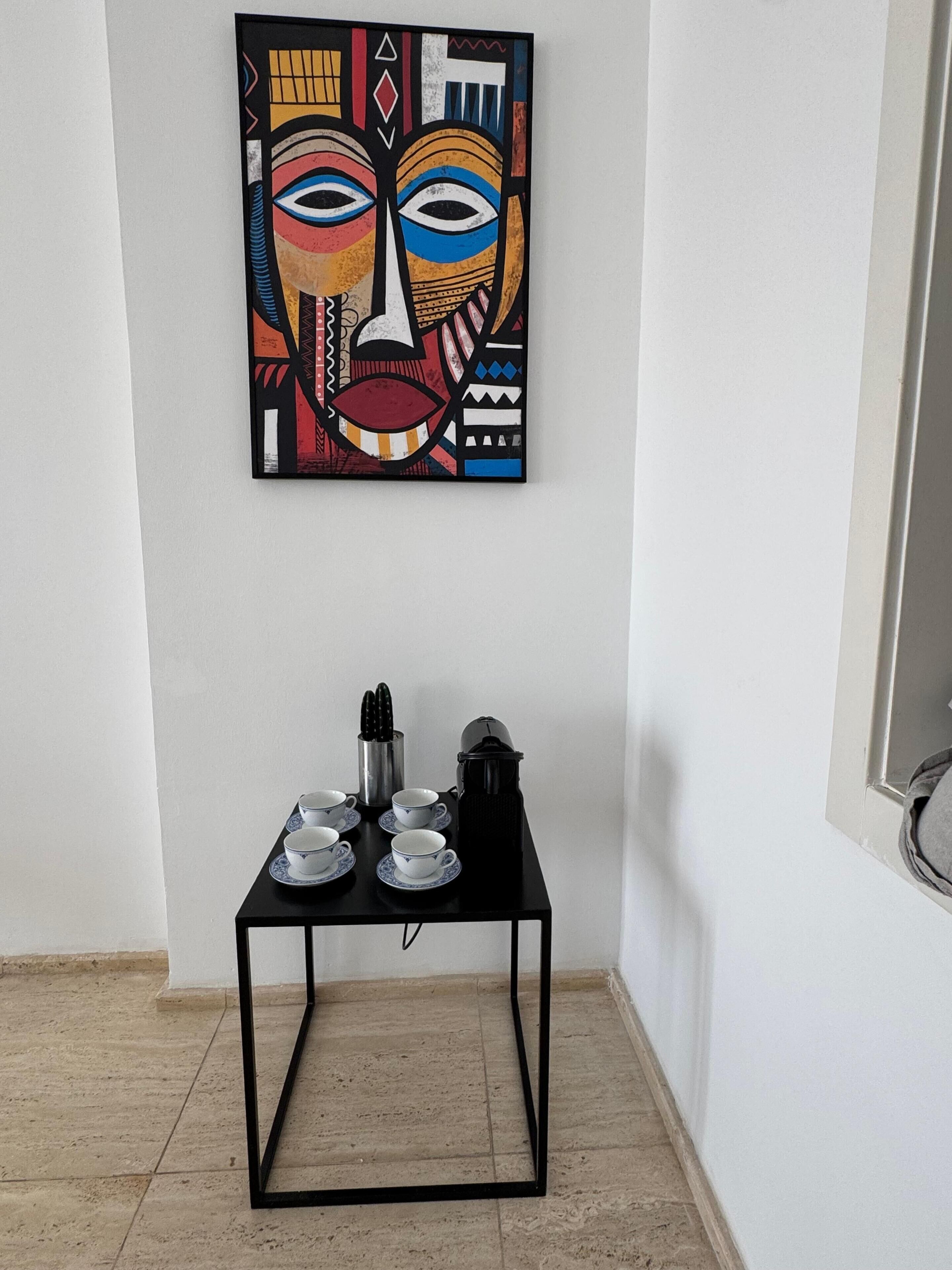 Um quarto com uma mesa de metal preta, paredes brancas e uma pintura abstrata colorida acima.