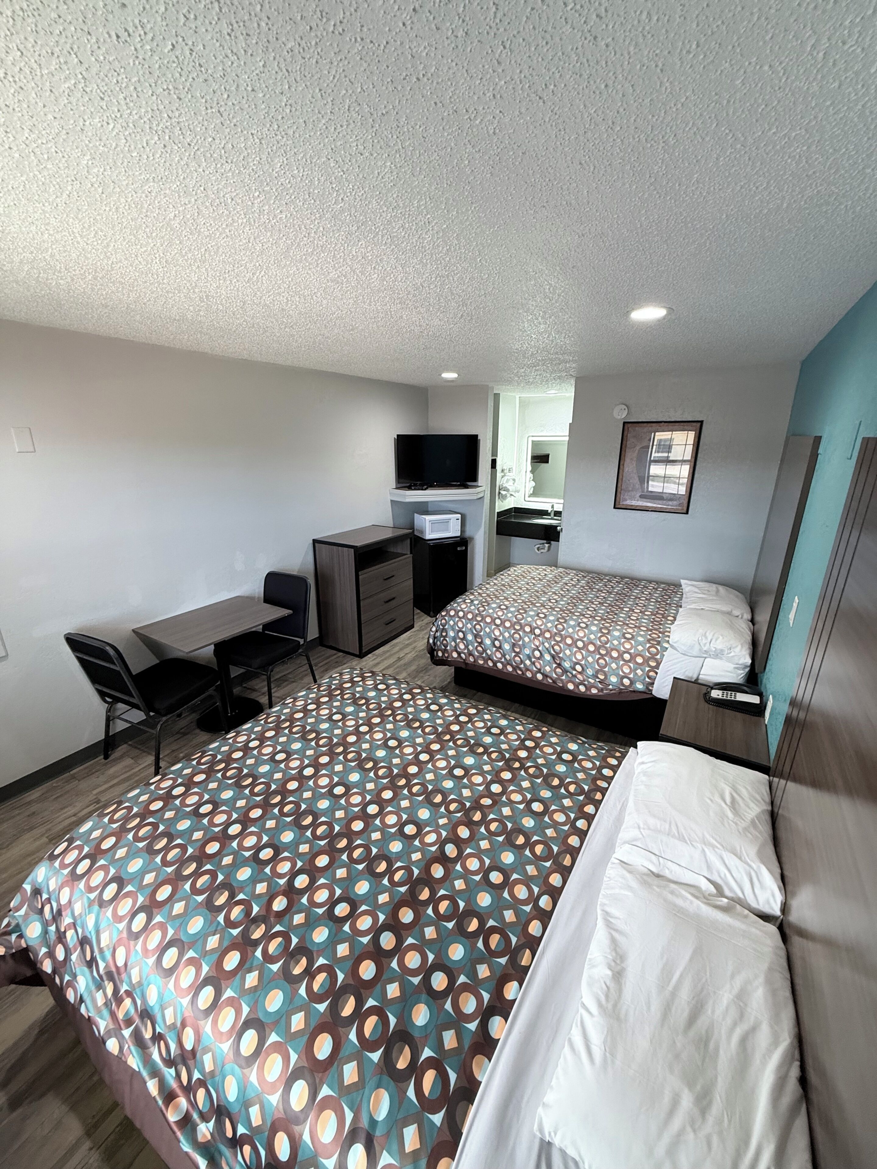A hotel room with two beds, a desk, a TV, and a bathroom.