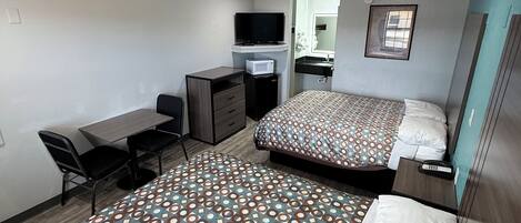 A hotel room with two beds, a desk, a TV, and a bathroom.