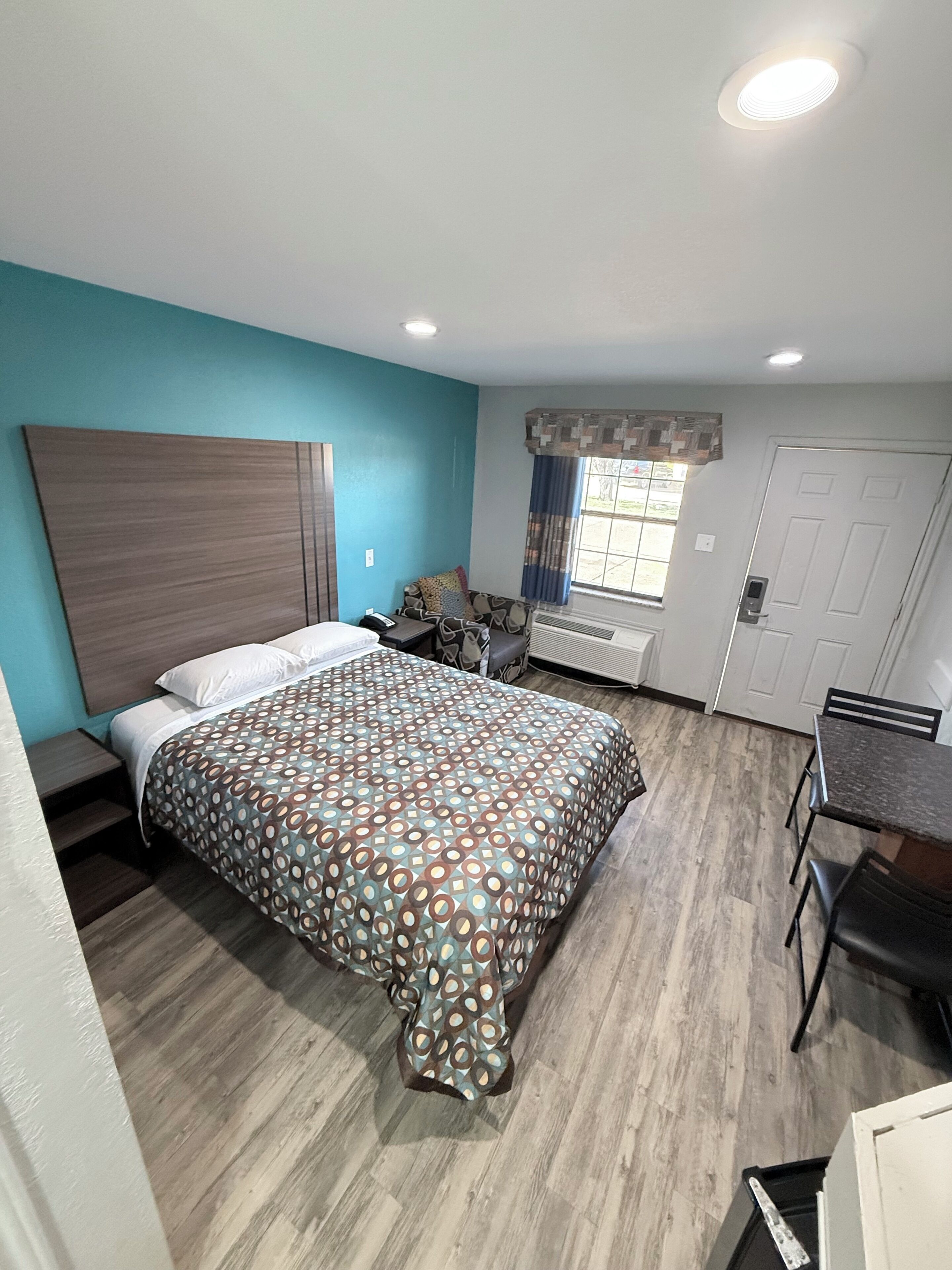 A room with a bed, a desk, a chair, a window with curtains, and a door.