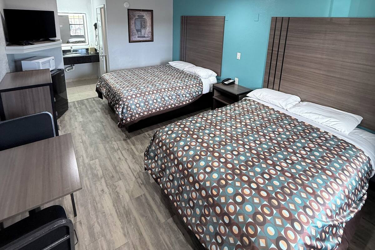 A hotel room with two beds, a desk, a TV, and a bathroom visible in the background.
