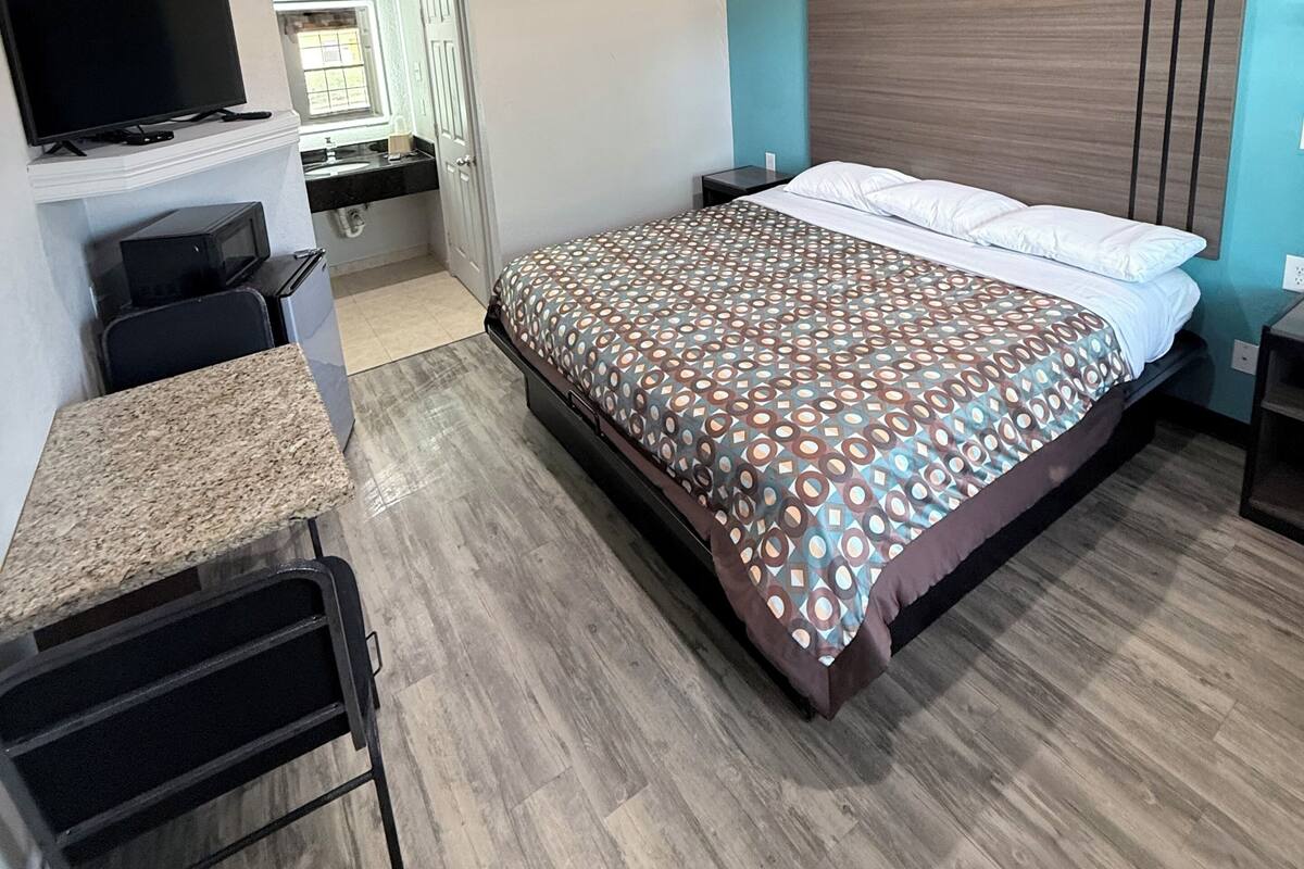 A hotel room with a bed, a desk, a television, and a bathroom visible through an open door.