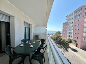 A balcony with a table and chairs, an air conditioning unit, and a view of the sea and buildings. - Cozy Stay in This Seaside Flat (Lignano Sabbiadoro)