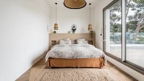 Un dormitorio con una cama grande, una lámpara colgante, una ventana con vistas y una mesita de noche con una planta.