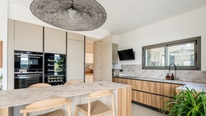 Una cocina moderna con encimera de mármol, taburetes de bar de madera, una isla grande y un televisor montado en la pared.