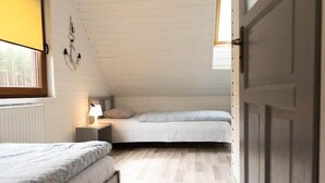 Ein kleines Schlafzimmer im Dachgeschoss, mit schrägem Dach, einem Fenster mit gelbem Rollo, einem Nachttisch mit Lampe und einer Tür rechts.