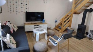 Ein gemütliches Wohnzimmer mit einer Couch, einem Fernseher, einer Holztreppe und einem Kamin.